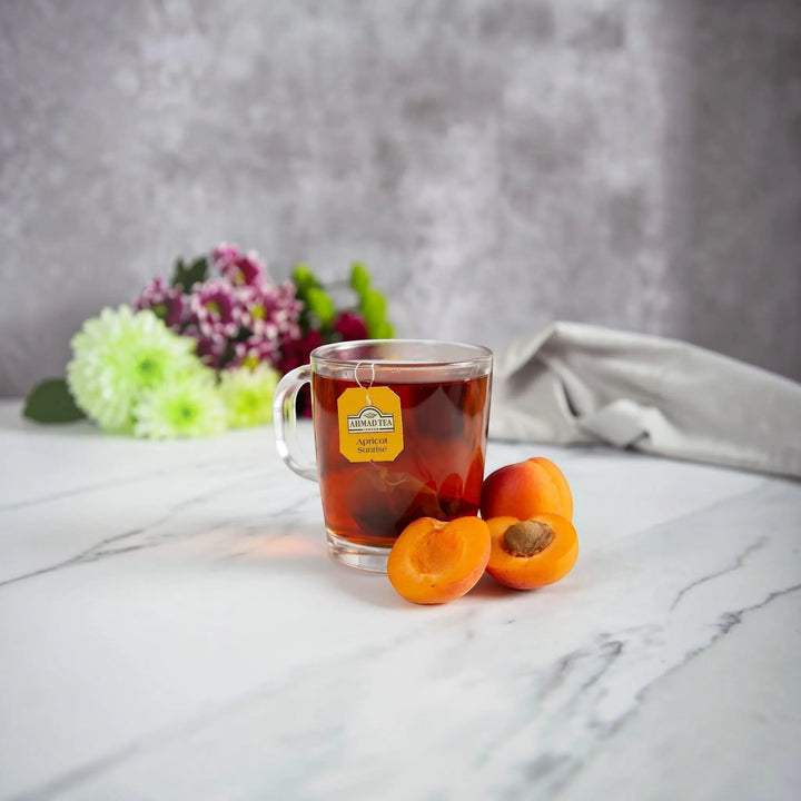 Delikatesi i tako to... Ahmad Tea Apricot Sunrise fruit tea in a glass mug with fresh apricot halves on a marble table