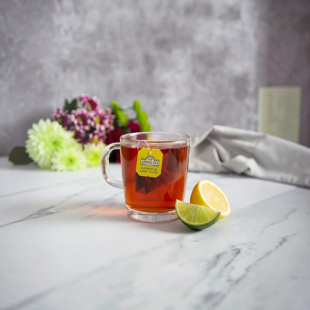 Ahmad Tea Lemon and Lime Twist fruit tea in a glass mug with fresh lemon and lime slices from Delikatesi i tako to...