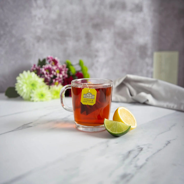 Ahmad Tea Lemon and Lime Twist fruit tea in a glass mug with fresh lemon and lime slices from Delikatesi i tako to...