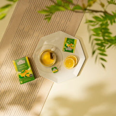Delikatesi i tako to... Ahmad Tea lemon green tea box, tea bag in a glass cup, and fresh lemon slices on a plate.