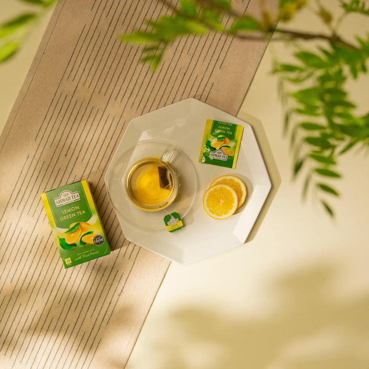 Delikatesi i tako to... Ahmad Tea lemon green tea box, tea bag in a glass cup, and fresh lemon slices on a plate.