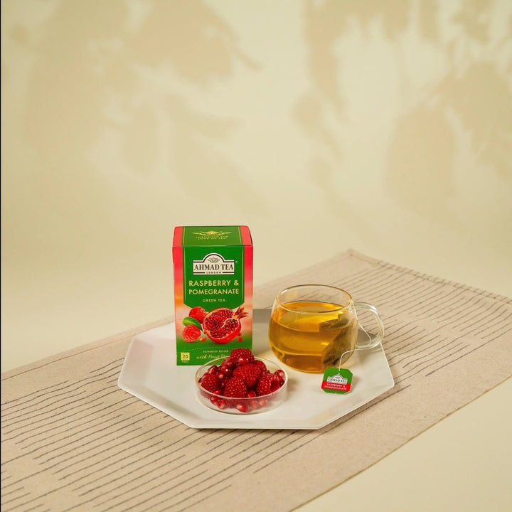 Delikatesi i tako to... Ahmad Tea Raspberry and Pomegranate green tea box with a cup and fresh fruit on a plate