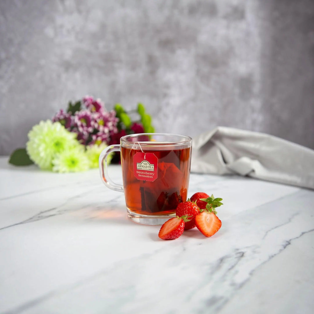 Delikatesi i tako to... Ahmad Tea Strawberry Sensation fruit tea bag steeping in a glass mug with fresh strawberries
