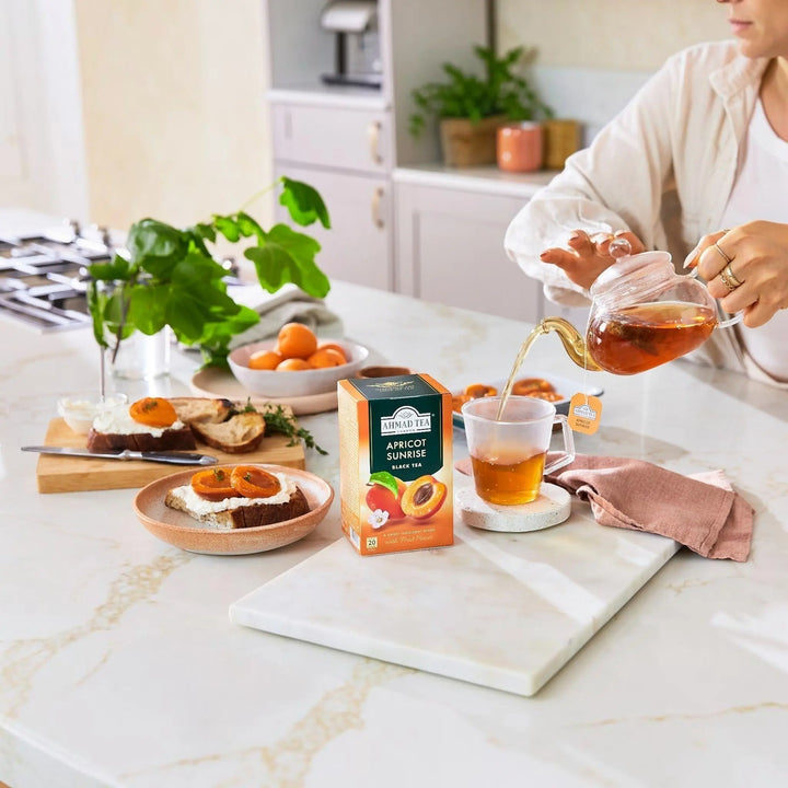 Delikatesi i tako to... Ahmad Tea Apricot Sunrise black tea box with tea being poured into a cup on a kitchen counter