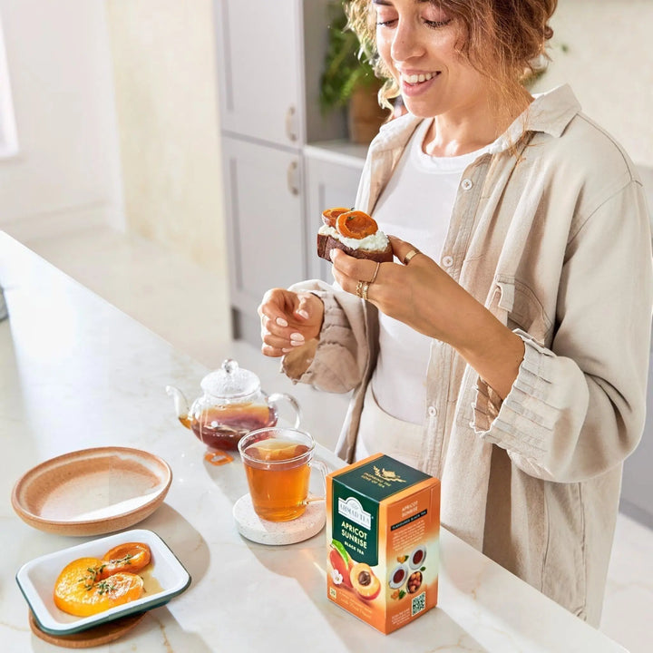 Delikatesi i tako to... Ahmad Tea Apricot Sunrise black tea box with a woman enjoying tea and apricot toast
