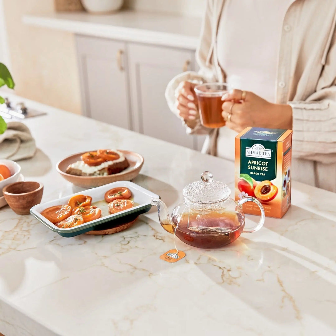 Delikatesi i tako to... Ahmad Tea Apricot Sunrise black tea box with a glass teapot and fresh apricots on a table