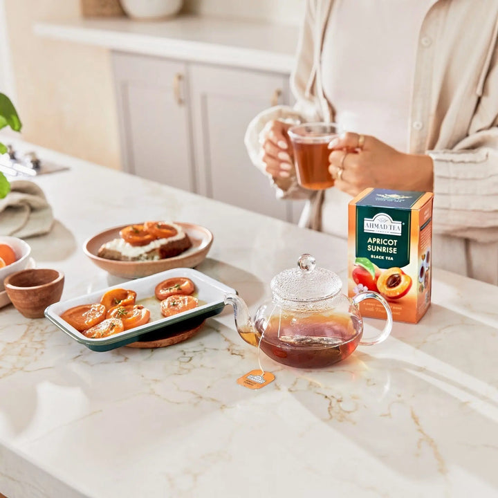 Delikatesi i tako to... Ahmad Tea Apricot Sunrise black tea box with a glass teapot and fresh apricots on a table