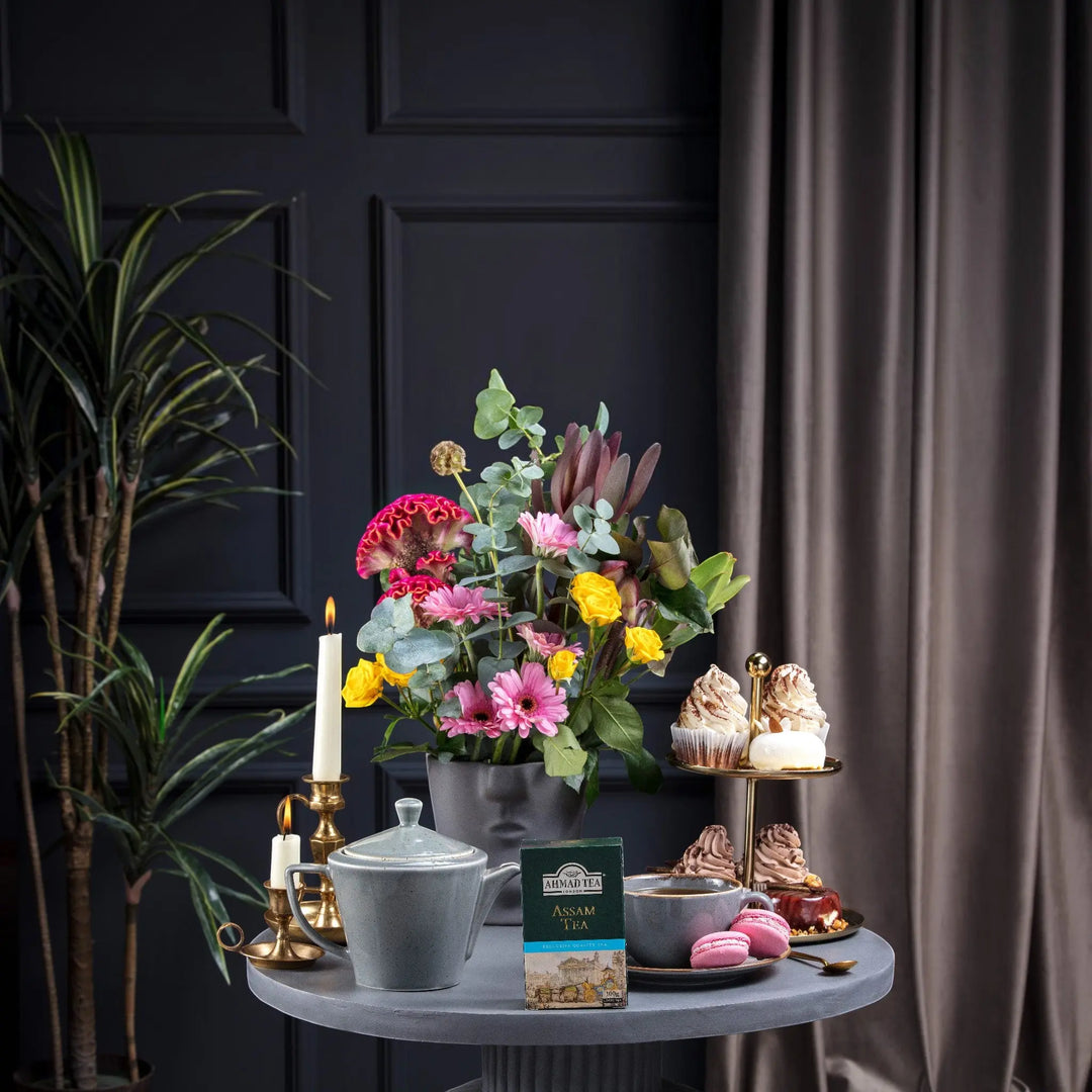 Delikatesi i tako to... Ahmad Tea Assam loose leaf tea box on a table with a teapot, cupcakes, and flowers