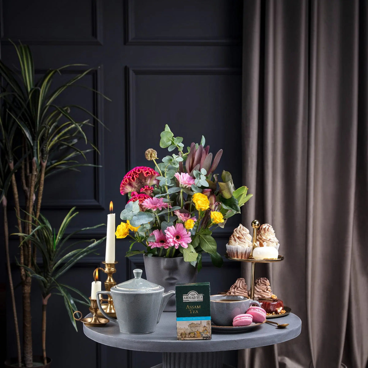 Delikatesi i tako to... Ahmad Tea Assam loose leaf tea box on a table with a teapot, cupcakes, and flowers