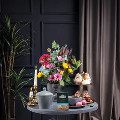 Delikatesi i tako to... Ahmad Tea Assam loose leaf tea box on a table with a teapot, cupcakes, and flowers