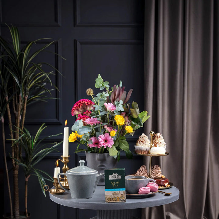 Delikatesi i tako to... Ahmad Tea Assam loose leaf tea box on a table with a teapot, cupcakes, and flowers