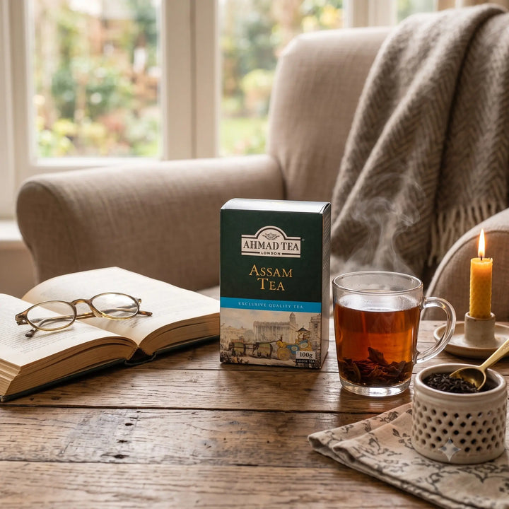 Delikatesi i tako to... Ahmad Tea Assam loose leaf tea box next to a steaming glass cup on a rustic wooden table.