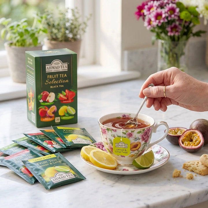 Delikatesi i tako to... Ahmad Tea Fruit Tea Selection box with tea bags, floral cup, and fresh lemon and lime slices.