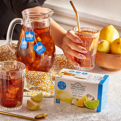 Delikatesi i tako to... Ahmad Tea Lemon & Lime cold brew iced tea box with a glass pitcher and fresh citrus slices.