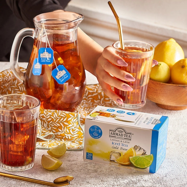 Delikatesi i tako to... Ahmad Tea Lemon & Lime cold brew iced tea box with a glass pitcher and fresh citrus slices.