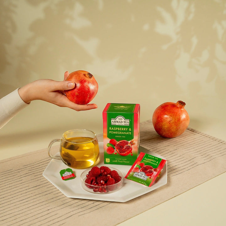 Delikatesi i tako to... Ahmad Tea Raspberry & Pomegranate green tea box with tea bags, fresh fruit, and a glass cup.