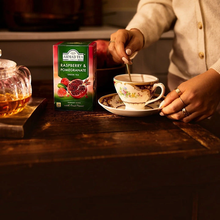 Delikatesi i tako to... Ahmad Tea Raspberry and Pomegranate green tea box next to a floral teacup being stirred