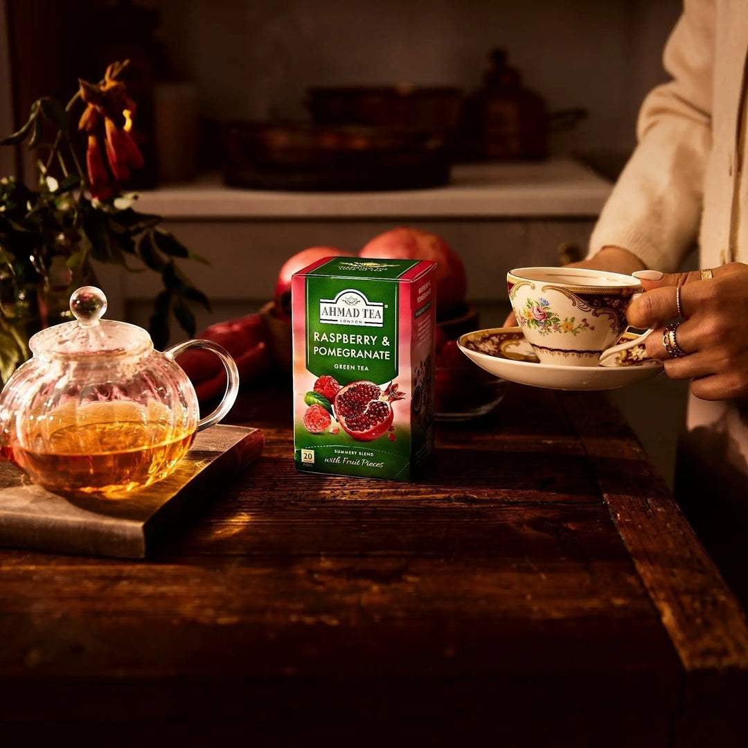 Delikatesi i tako to... Ahmad Tea Raspberry and Pomegranate green tea box with fruit pieces on a wooden table.