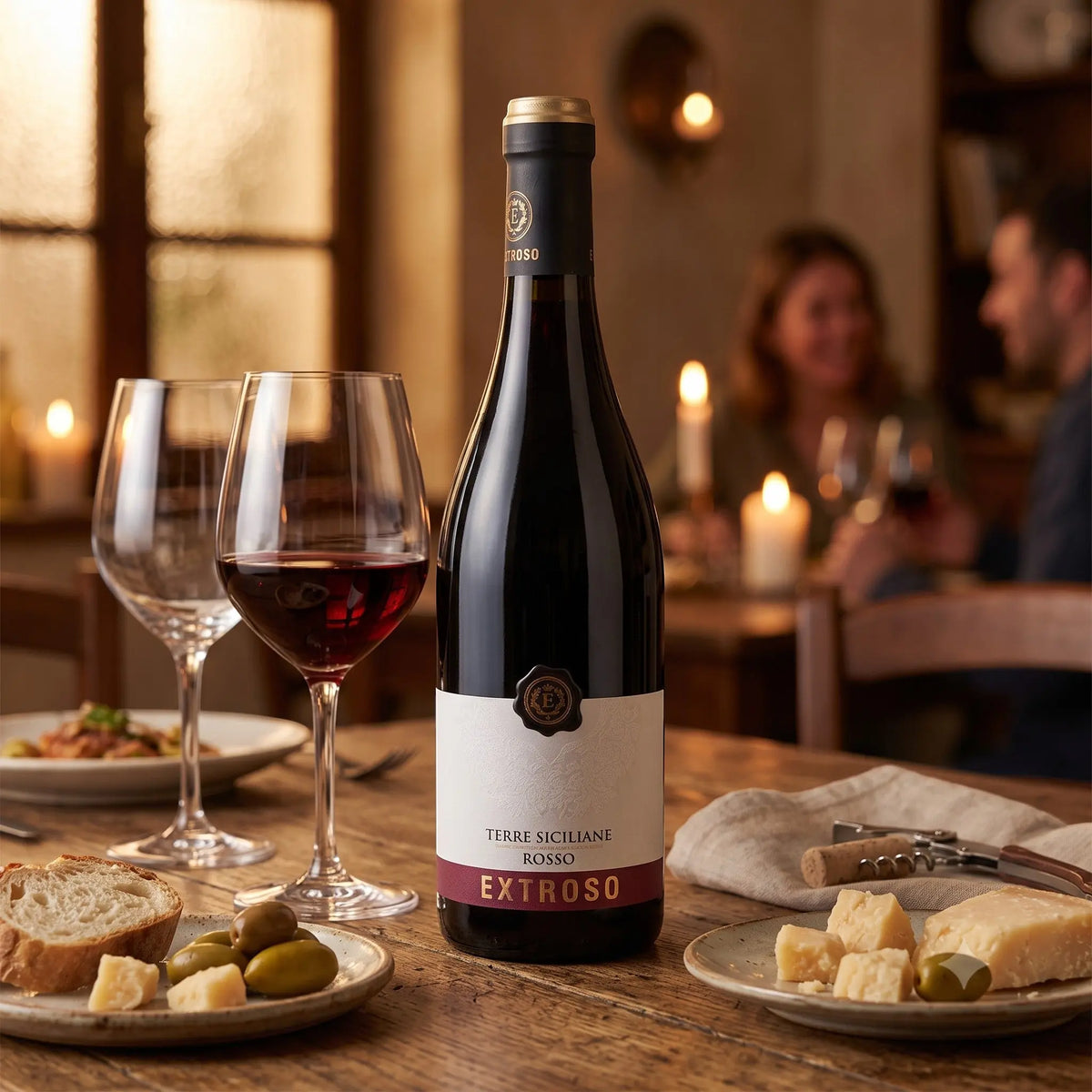Delikatesi i tako to... Extroso Terre Siciliane red wine bottle on a rustic dining table with wine glasses and appetizers.