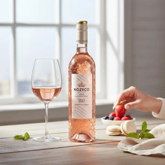 Delikatesi i tako to... Nozeco alcohol-free rose wine bottle with a glass, strawberries, and macarons on a table.