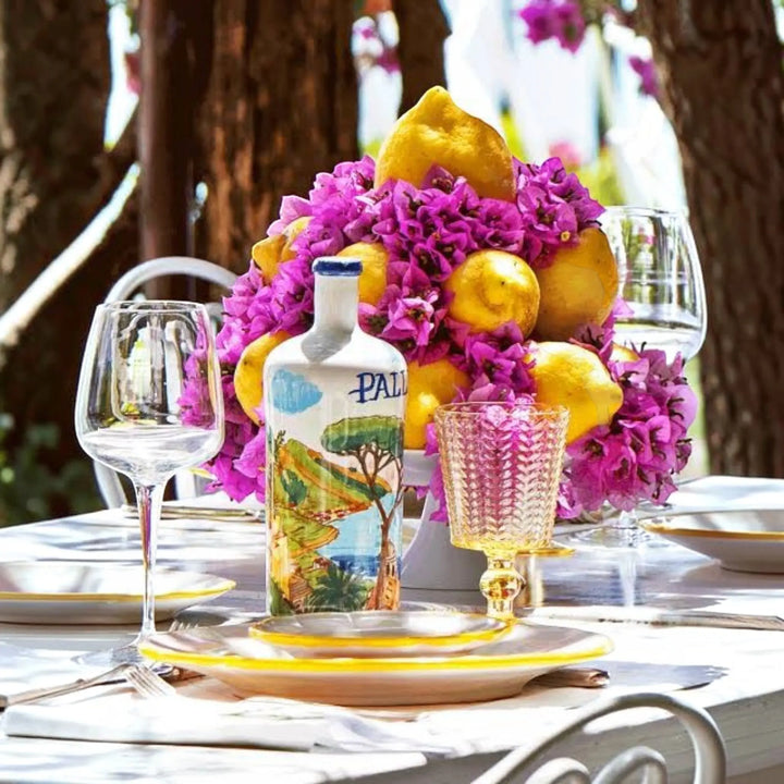 Delikatesi i tako to... Pallini Limoncello bottle with Amalfi coast illustration, surrounded by lemons and flowers.