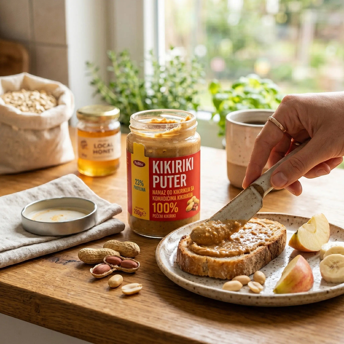 Delikatesi i tako to... Pellito crunchy peanut butter spread being spread on a slice of bread with fruit on a table.