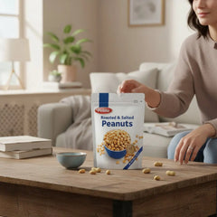 Delikatesi i tako to... Pellito roasted and salted peanuts in a 150g pouch, held by a woman in a cozy living room.