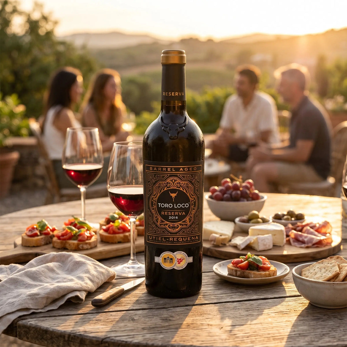 Delikatesi i tako to... Toro Loco Reserva red wine bottle on a table with appetizers at a sunset outdoor gathering.